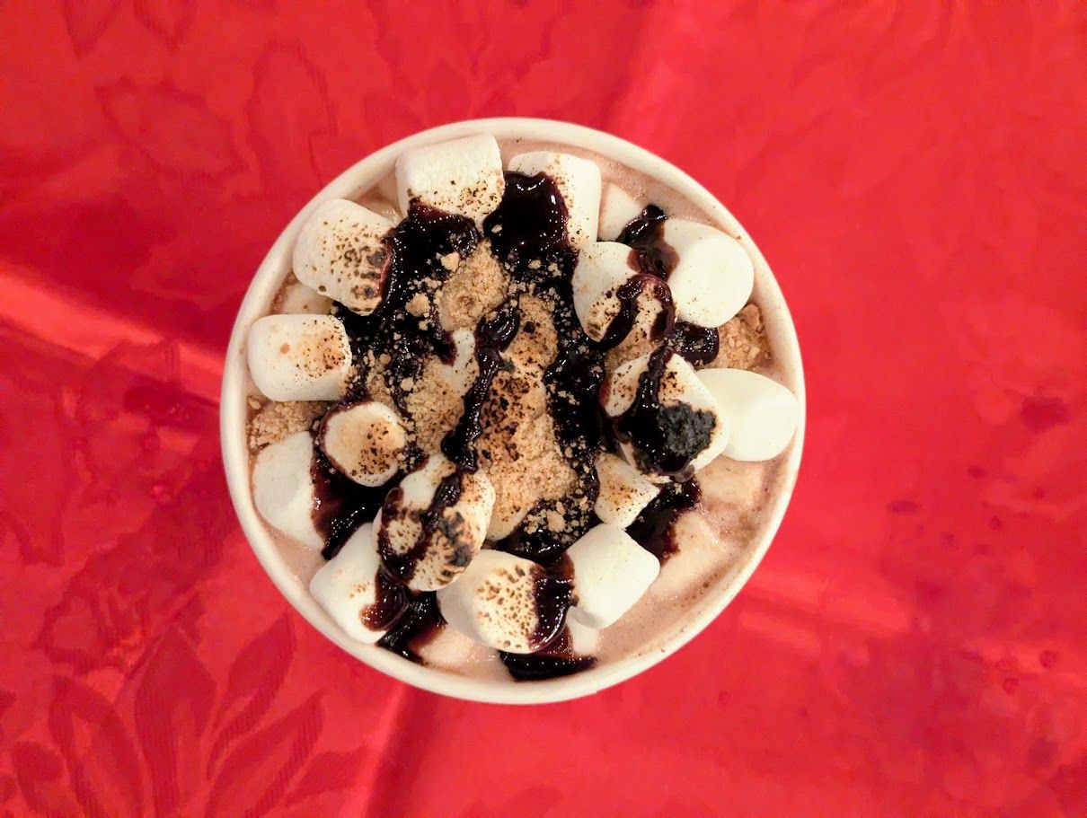 Hot chocolate topped with marshmallows and a berry drizzle