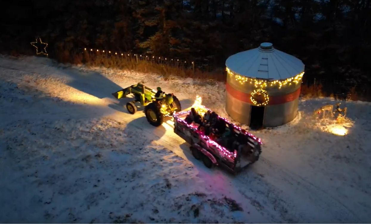 A tractor pulling the wagon past a lit grain bin in the snow